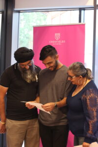 Three adults look at a sheet of paper together at a school event, with a bright pink Crosfields School banner in the background.