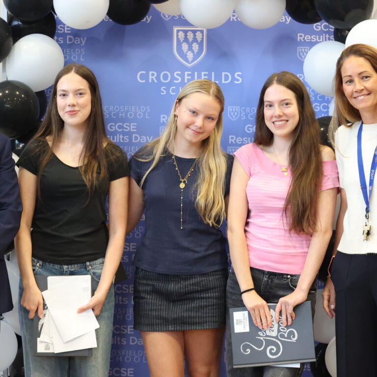 Five people posing for a group photo at Crosfields School GCSE Results Day, in front of a blue backdrop with balloons and the school logo.